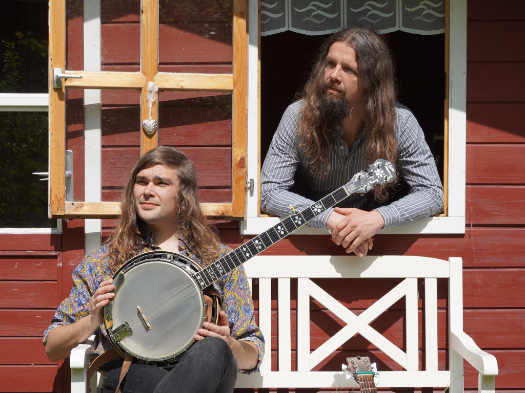Steffen Thede und Beni Feldmann, Steffen sitzt auf der Bank und hält sein Banjo, neben ihm lehnt Benis Gitarre, Beni schaut aus dem Fenster